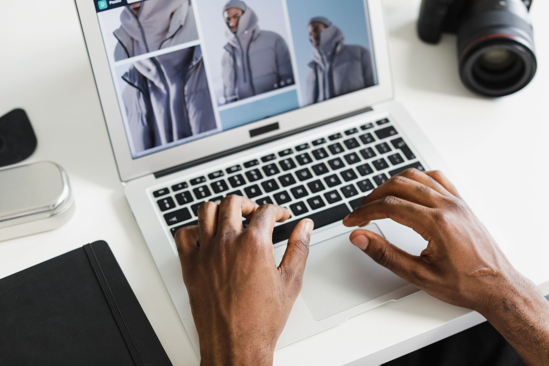 a photographer typing on a laptop with a camera on the desk beside them