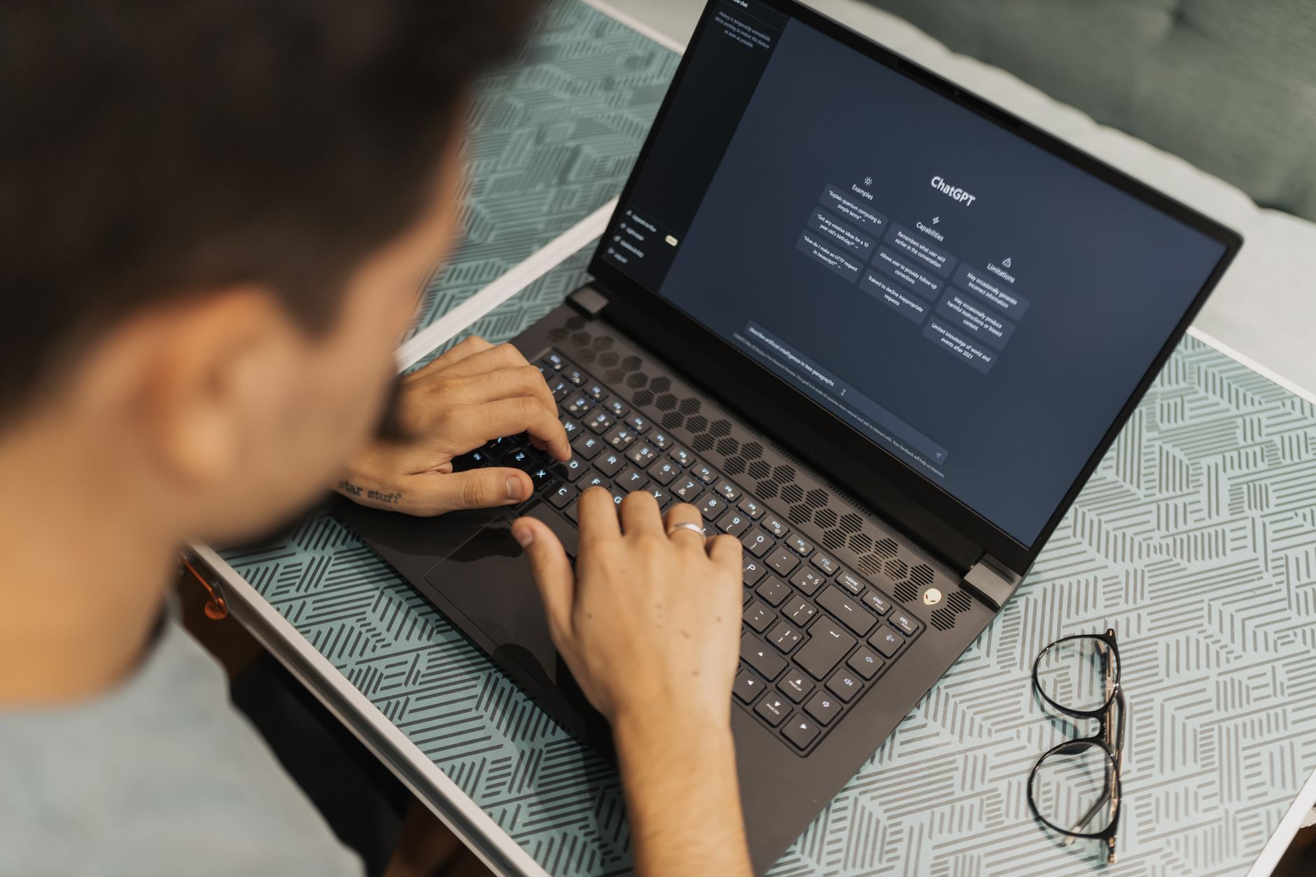 a person typing on a laptop with an AI chatbot interface open while surrounded by podcast notes and a microphone