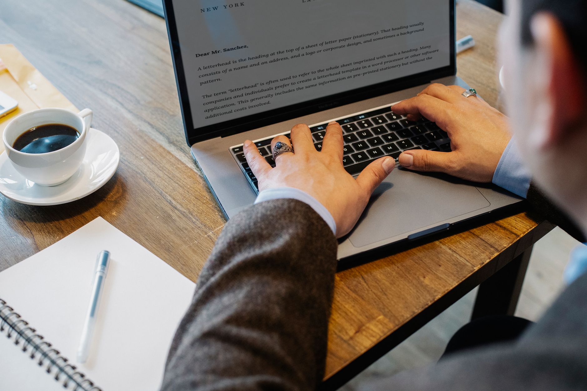 a writer typing on a laptop beside an open notebook and coffee cup